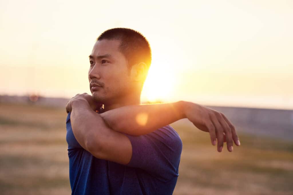 man stretching his arms before going for a solo run outside on a sunny morning